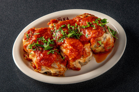 6 Stuffed Cabbage on a serving plate with red sauce a basil on top.