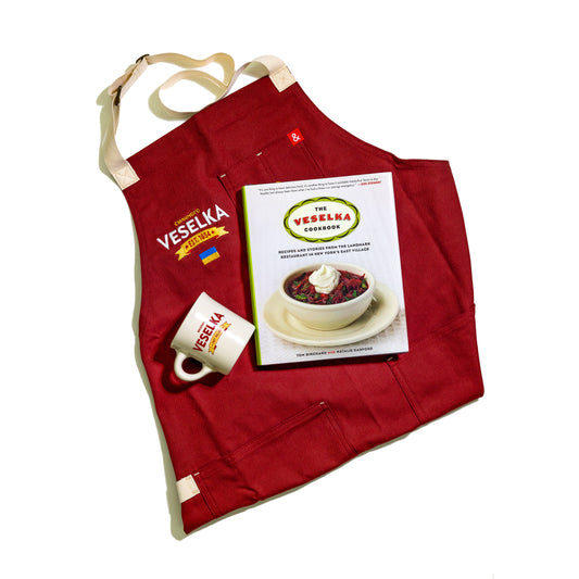 Veselka apron, mug and cookbook. Apron is red with veselka logo and small Ukrainian flag embroidered on the chest