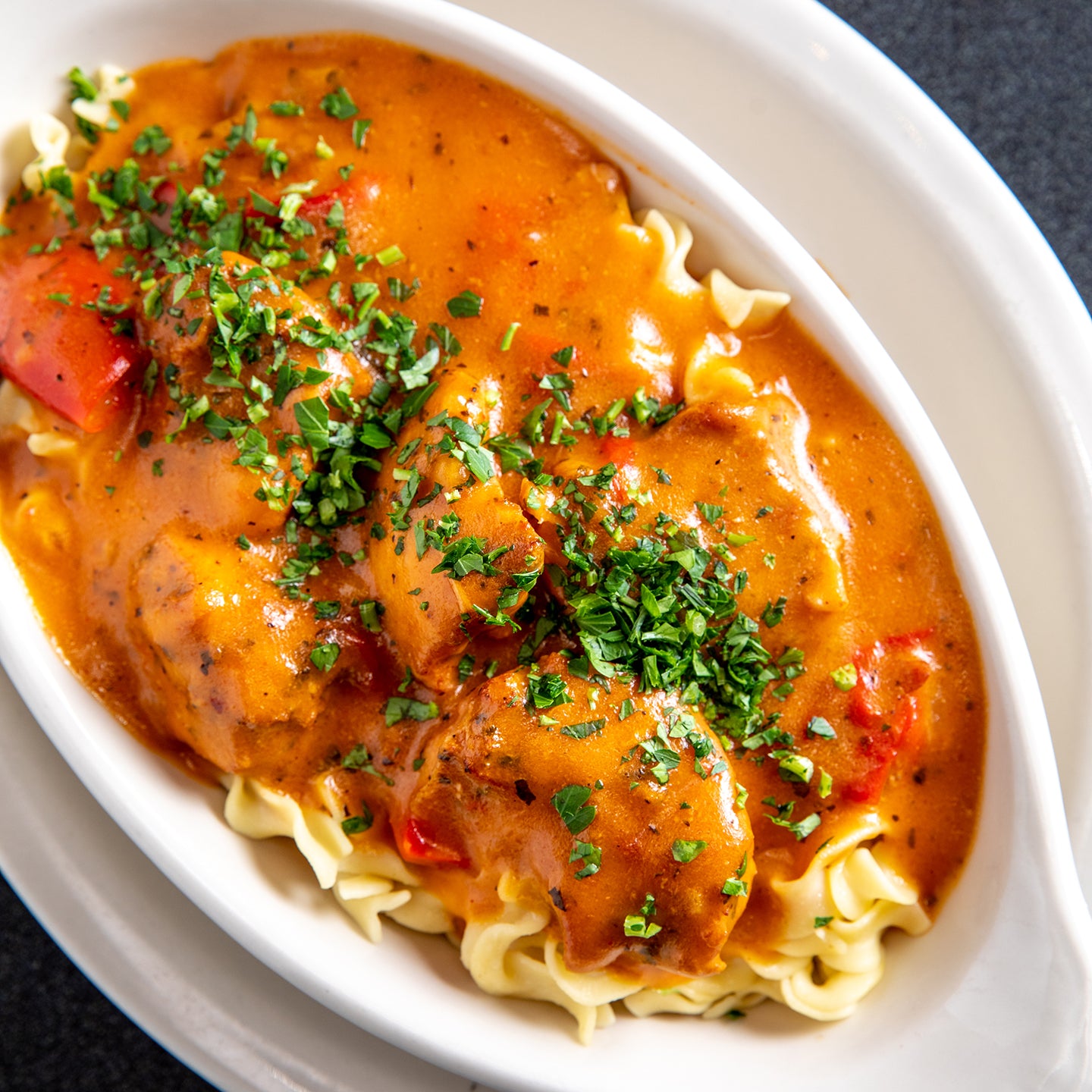 Chicken Paprikash with parsley sprinkled over the top, over egg noodles 